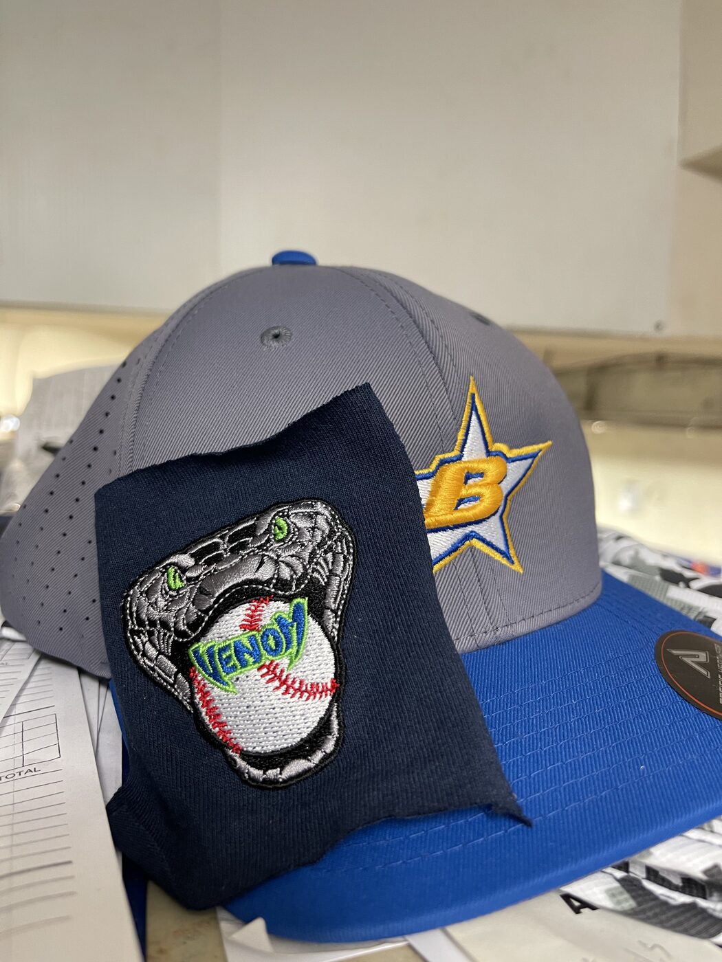 Gray and royal blue cap with a Venom baseball glove patch and gold B star logo.