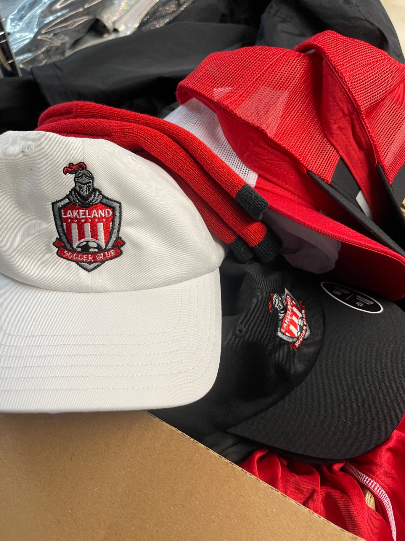 Assorted Lakeland Soccer Club embroidered hats in white, red, and black.