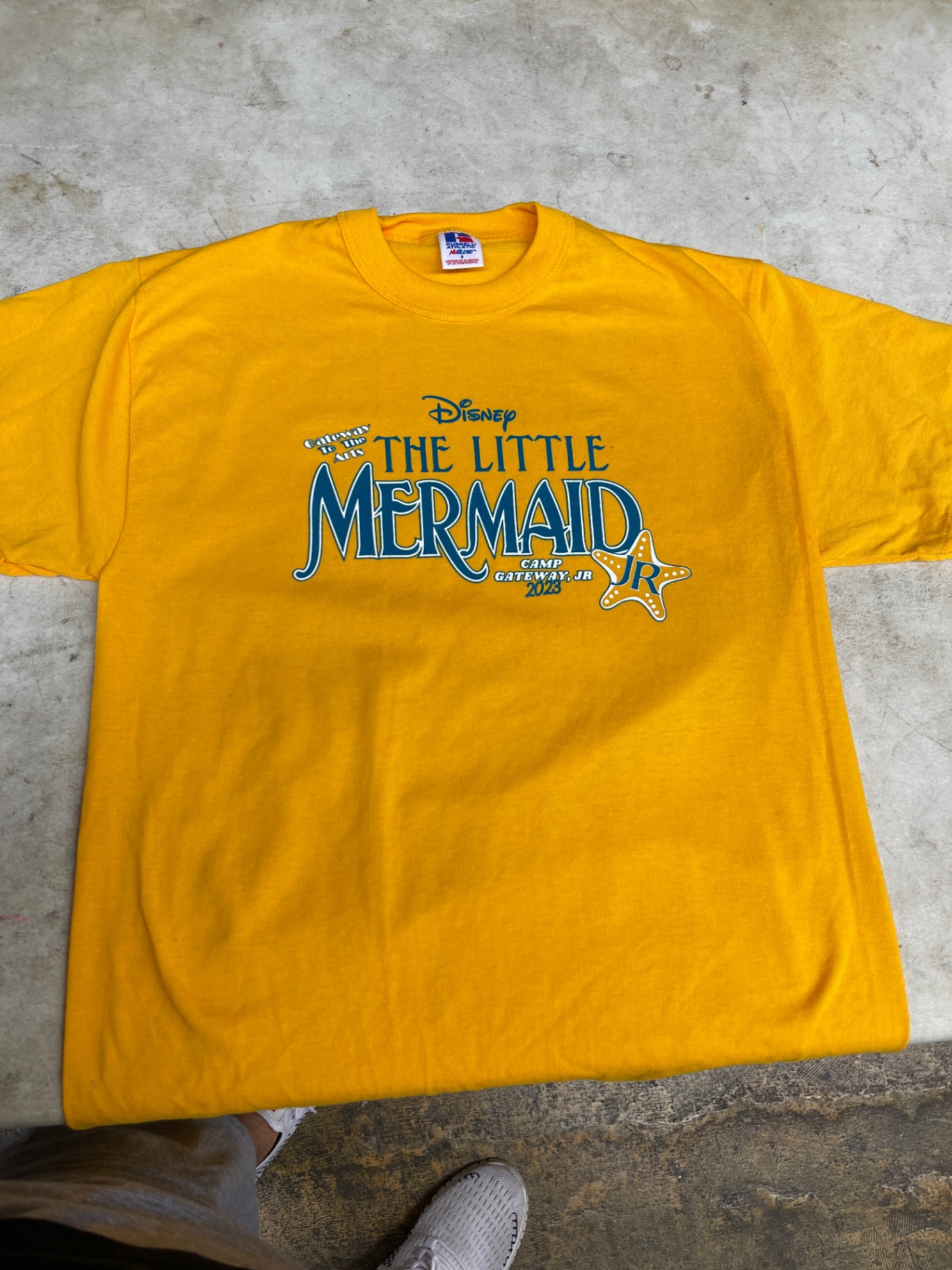 Yellow Disney The Little Mermaid Jr camp shirt laid flat.