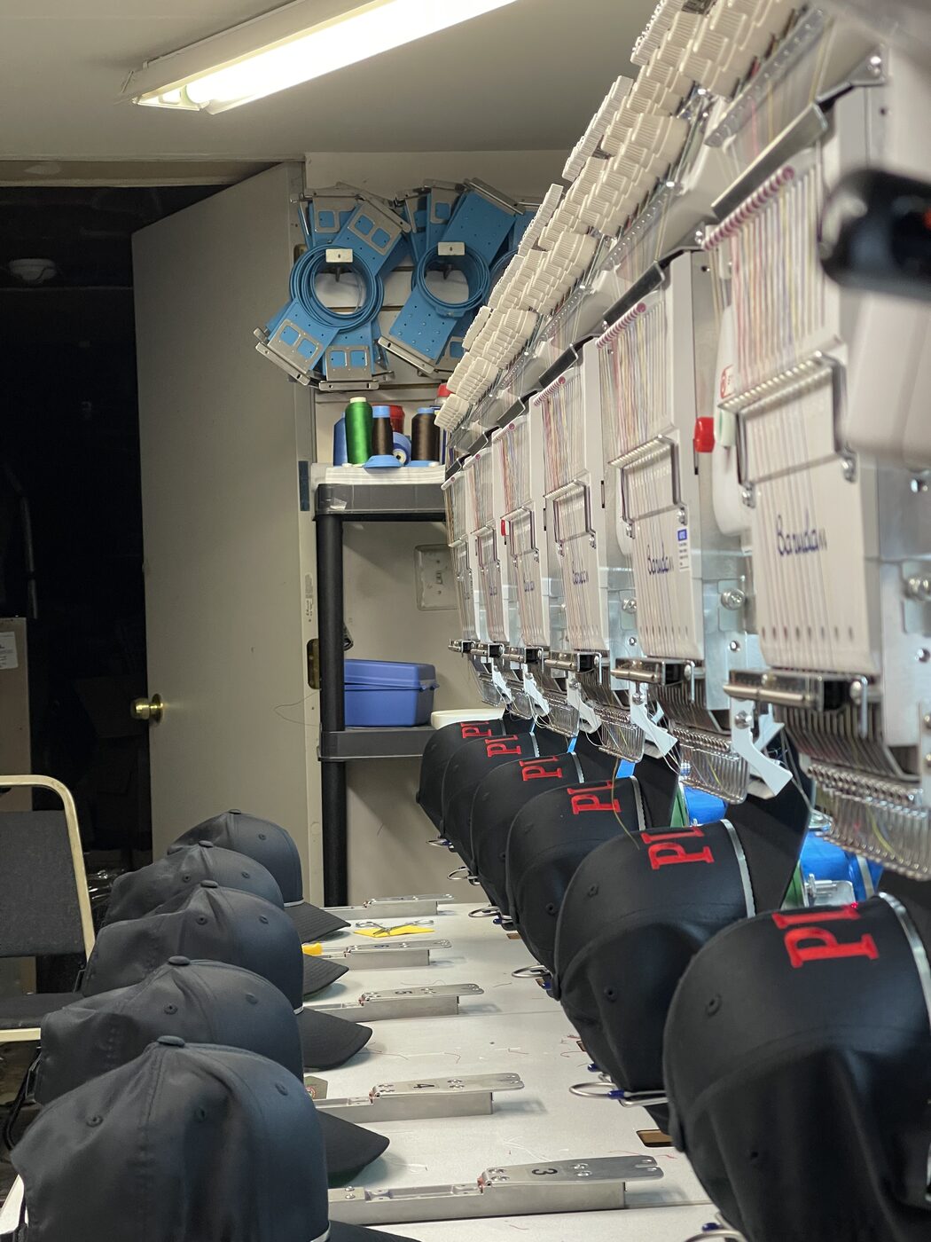 Row of black caps being embroidered in production on a multi-head Barudan embroidery machine.